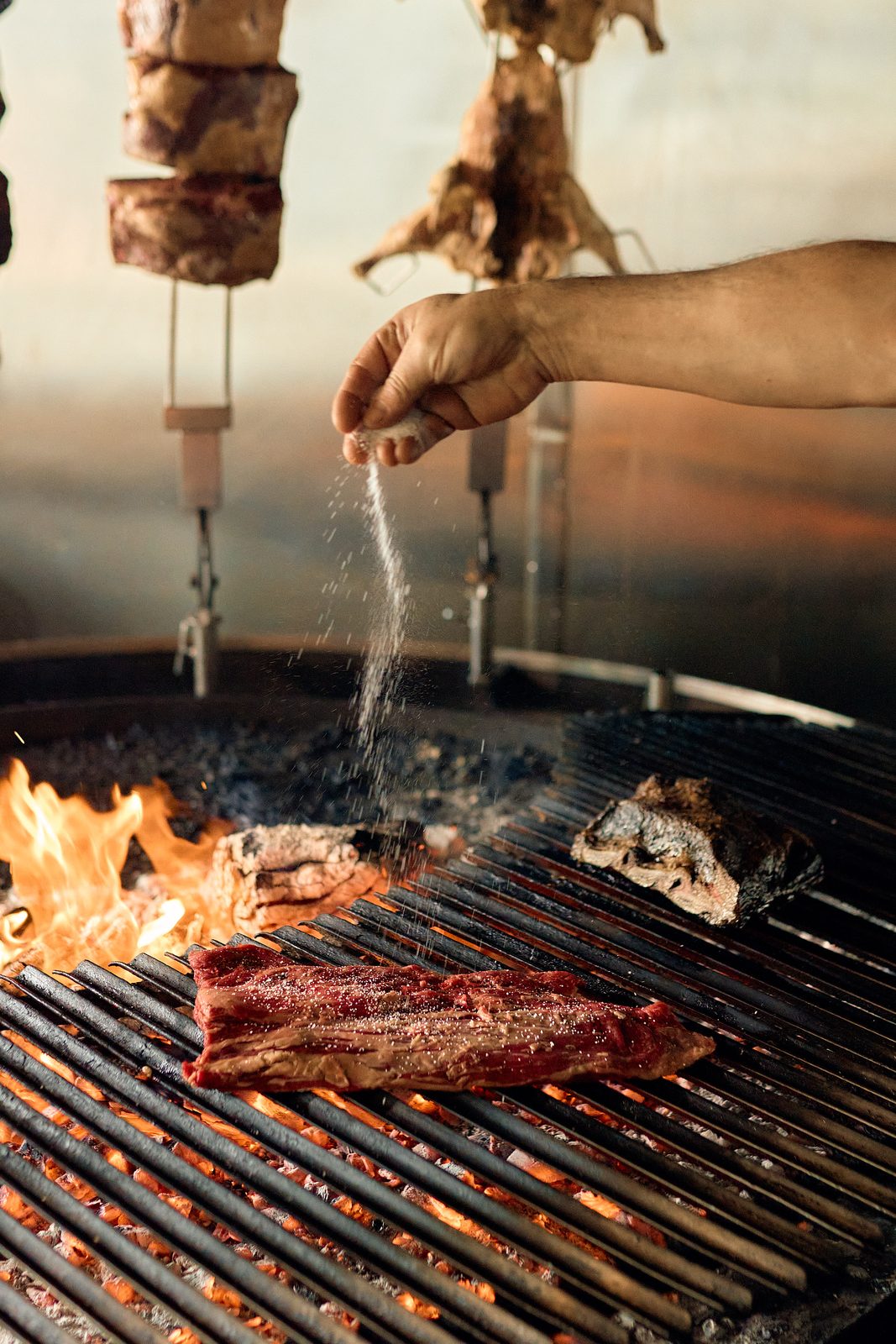 Salting a cut of beef over the open fire grill at Graziano's