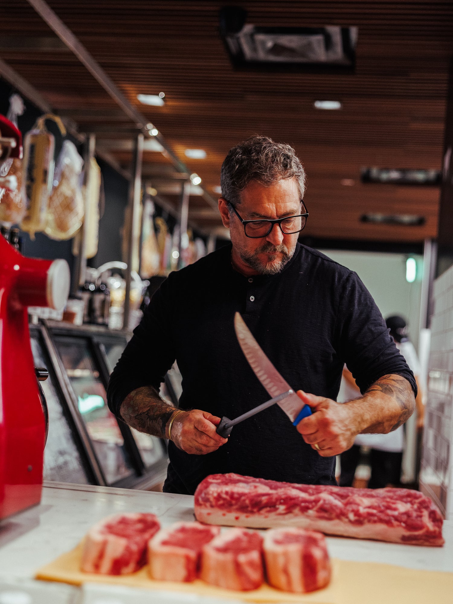 Man in a kitchen sharpening a knife with raw meat on a cutting board.