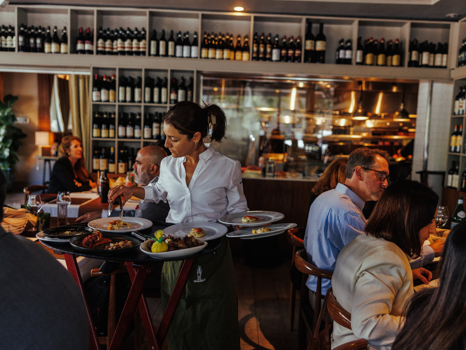 Dining scene in a restaurant with people seated at tables and a woman serving food.