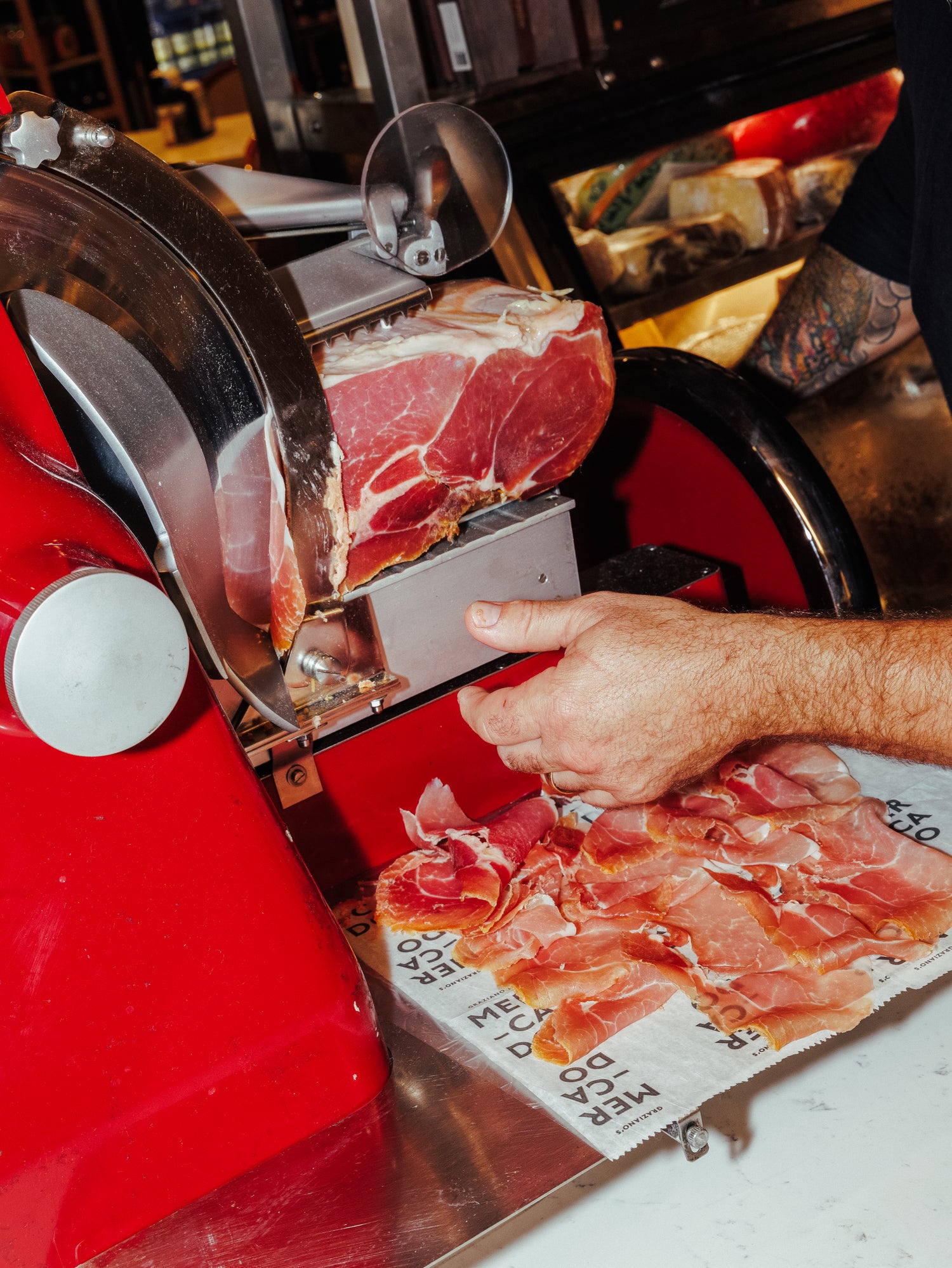 Person using a red meat slicer to cut ham with a close-up view of the slicing process.