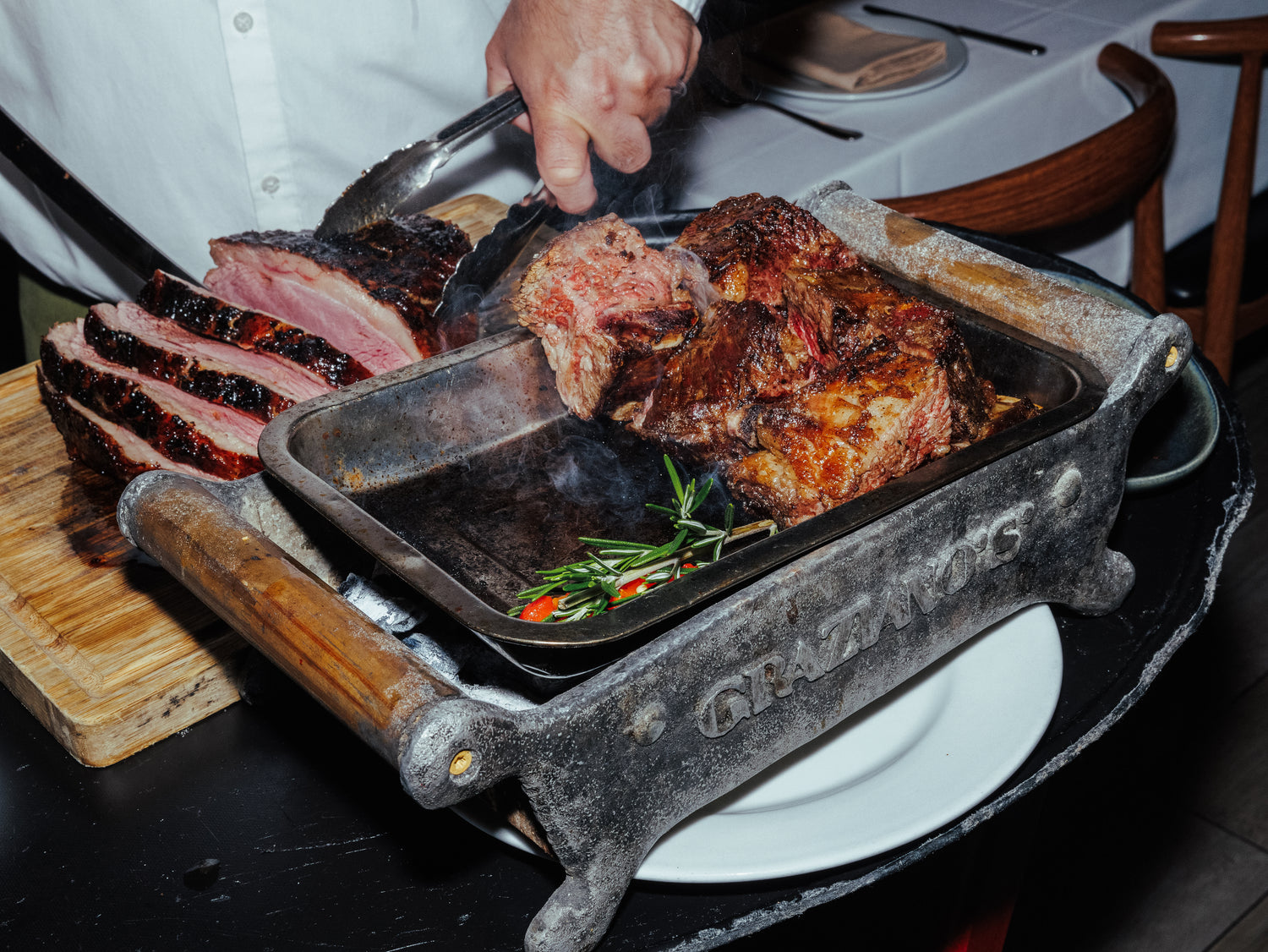 Grilled meat on a cast iron pan with a wooden handle, set on a dining table.