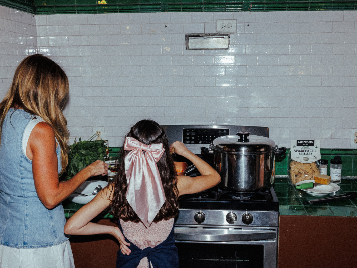 Two women in a kitchen with a pot on the stove and various items on the counter.
